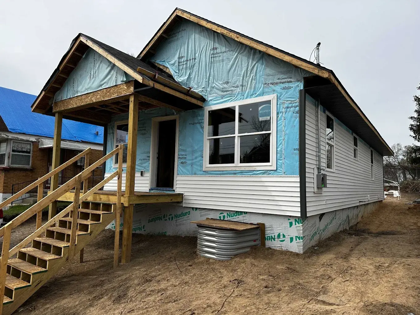 ADU mid-construction showing house wrap, vinyl siding installation, and front porch framing