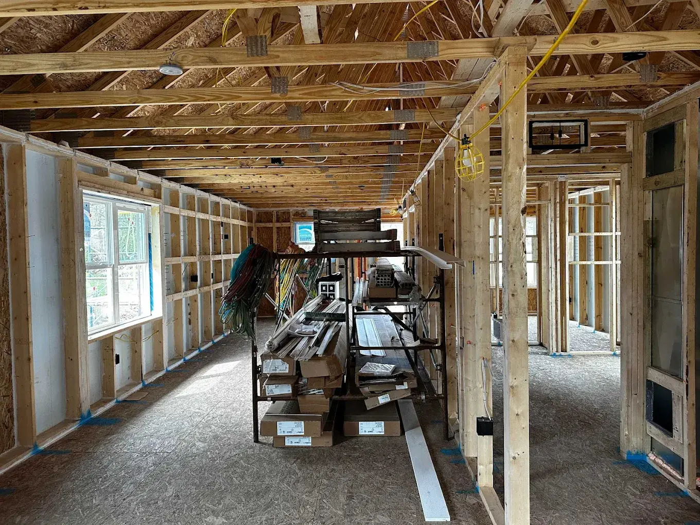 ADU interior framing with roof trusses, stud walls, and construction materials staged on site
