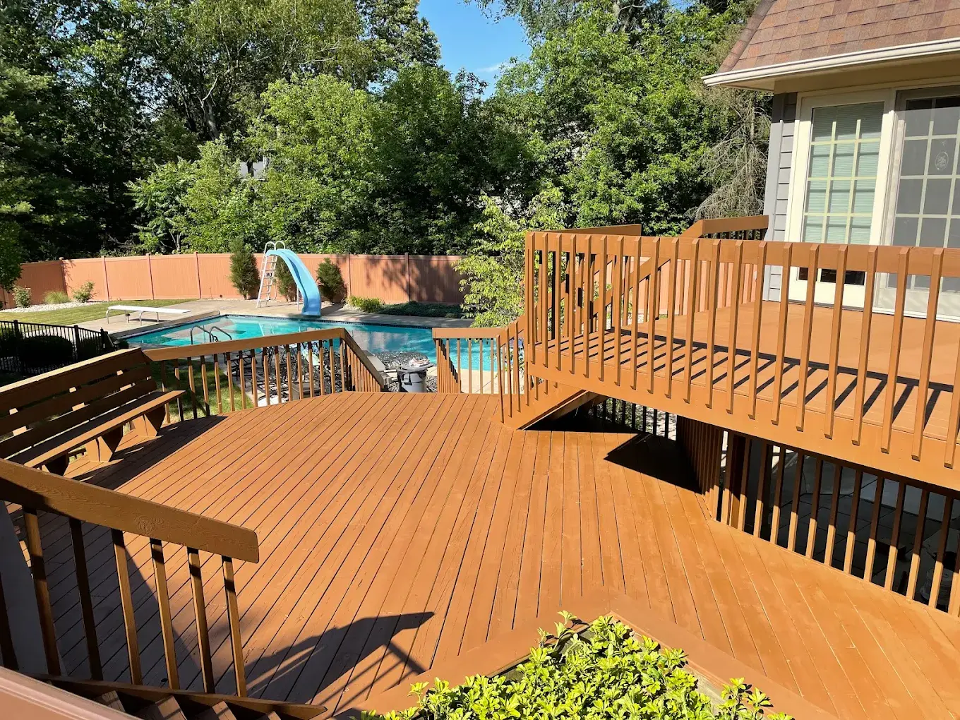 Multi-level wood deck with built-in benches and railing overlooking backyard pool