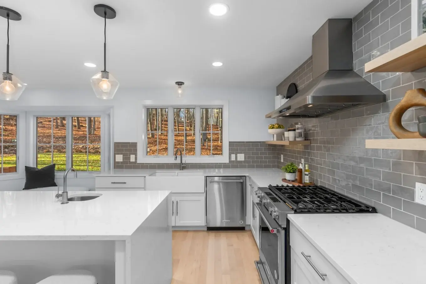 Remodeled kitchen with stainless steel range, gray tile backsplash wall, pendant lighting, and quartz countertop island